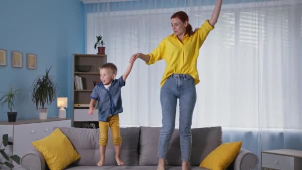 Family fun, young cheerful mom has fun with her little son and jumping on the couch in room at home — Stock Video