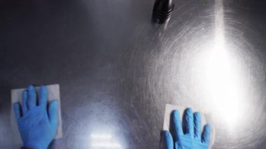 Yemek hazırladıktan sonra mutfakta mavi eldiven takan bir aşçı yemekle temas ettikten sonra mutfak yüzeylerini temizliyor. Birinci şahıstan en iyi görüntü. Çok yakından.