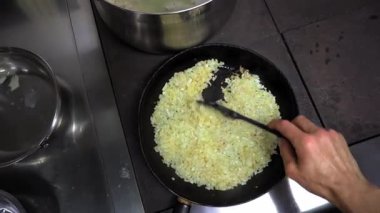 İnsan eli silikon kaşığı alır sıcak bir tavada sebze yağıyla ince doğranmış soğanları kızartır. Birinci şahıstan en iyi görüntü. Büyük yakın çekim.