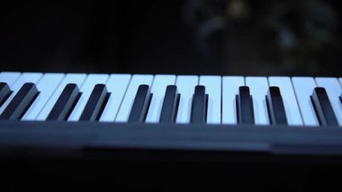 Kamera piyano klavyesinde ilerlerken, kamera kadınların onu çalarken ellerini yakalar. Kadın, belirgin kumaş dokusuna sahip gri uzun kollu bir ceket giyiyor. Büyük yakın çekim.