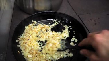 Silikon kaşıkla insan eli sıcak bir tavada sebze yağıyla ince ince doğranmış soğanları karıştırır. Birinci şahıstan en iyi görüntü. Büyük yakın çekim.