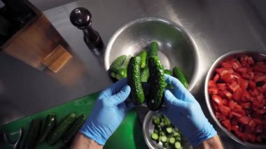 Mutfakta mavi eldivenli bir aşçı kesme tahtasından salatalık toplar, inceler ve paslanmaz çelik bir kaseye koyar. Birinci şahıstan en iyi görüntü. Büyük yakın çekim.