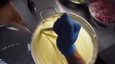 Mutfakta kesim masasında mavi eldiven giyen bir şef tencerede haşlanmış patates karıştırıyor. Birinci şahıstan en iyi görüntü. Büyük yakın çekim.