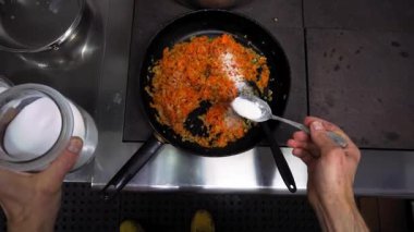 Bir şef gerekli malzemeleri kaşıkla sıcak bir tavada sebze yağıyla ince doğranmış soğan ve havuç haline getirir. Birinci şahıstan en iyi görüntü. Büyük yakın çekim.