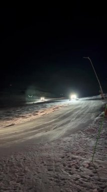 Gece, parlak ışıklı bir kar aracı kayak yamacından inerek, altındaki karı düzleştirir ve sıkıştırır. Yolu boyunca uzanan aşırı karları ortadan kaldırır ve güçlü spot ışıklarıyla onu aydınlatır.