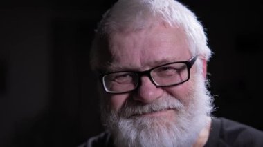 Gözlüklü gri saçlı adam iyi bir jest yapıyor. Koyu arkaplan, duygusal durumunu vurgulayan erkek figürüne şiddetle zıt düşüyor. Portre fotoğrafı. Aşırı yakın çekim.