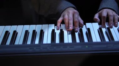 Kamera piyano klavyesinde tepeden tırnağa hareket ederken kamera, kadının ellerini çalarken yakalıyor. Kadın, belirgin kumaş dokusuna sahip gri uzun kollu bir ceket giyiyor. Büyük yakın çekim.