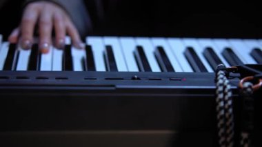 Kamera piyano klavyesinde ilerlerken, kamera kadınların onu çalarken ellerini yakalar. Kadın, belirgin kumaş dokusuna sahip gri uzun kollu bir ceket giyiyor. Büyük yakın çekim.
