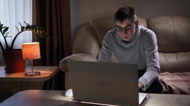 Oturma odasındaki evinde genç kız pencerenin yanındaki kanepede oturur ve dizüstü bilgisayarı üzerinde çalışır. Yanında bir gece lambası ve çiçekler var. Çocuk loş bir odada, penceresi açık.