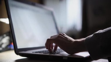 Kahve masasında duran dizüstü bilgisayarın klavyesinde yazan çocuk. Karanlık odada, pencereden gelen ışık klavyeye düşer ve çocuk ellerini tutar. Kamera karşıya geçiyor. Aşırı yakın çekim.