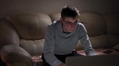 Oturma odasındaki evinde genç kız pencerenin yanındaki kanepede oturur ve dizüstü bilgisayarı üzerinde çalışır. Yanında bir gece lambası ve çiçekler var. Çocuk loş bir odada, penceresi açık.