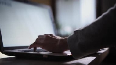 Çocuk sehpanın üzerinde duran bir dizüstü bilgisayarın klavyesinde yazmaya başladı. Karanlık odada, pencereden gelen ışık klavyeye düşer ve çocuk ellerini tutar. Aşırı yakın çekim.