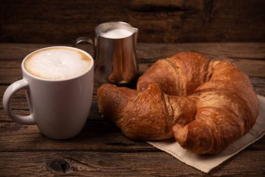 Taze tereyağlı kruvasan ve kırsal ahşap masada kahve. Yakın plan.