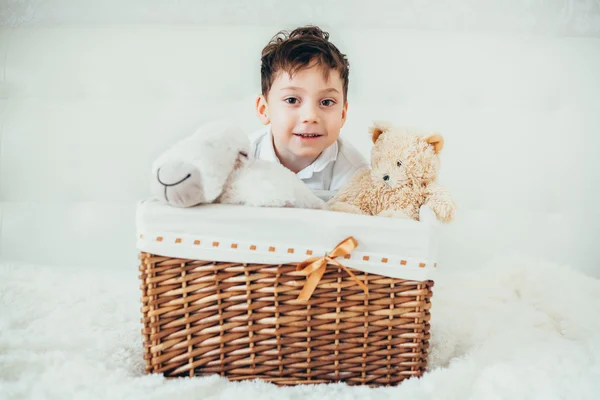 Menino escondido atrás de uma cesta com brinquedos macios — Fotografia de Stock