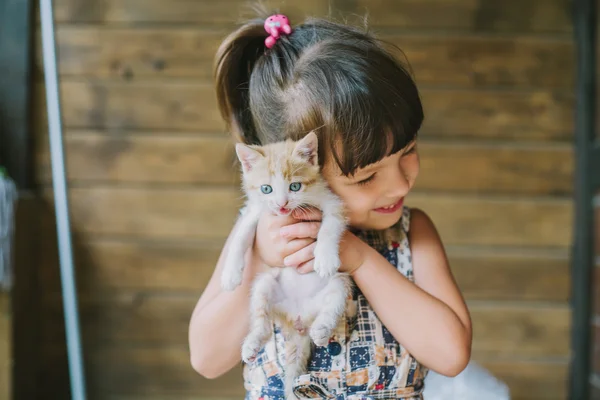 Fröhliches kleines Mädchen mit einer verängstigten Katze in den Händen — Stockfoto