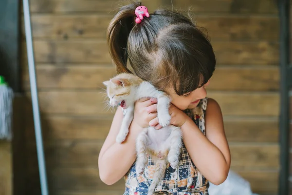 Fröhliches kleines Mädchen mit einer verängstigten Katze in den Händen — Stockfoto