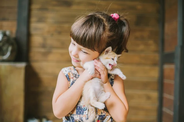 Fröhliches kleines Mädchen mit einer verängstigten Katze in den Händen — Stockfoto