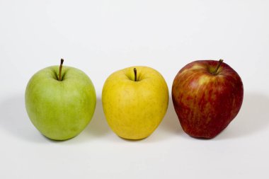 Beyaz arka planda üç sarı, kırmızı ve yeşil elma yan yana yerleştirilir..