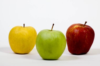 Beyaz arka planda üç sarı, kırmızı ve yeşil elma yan yana yerleştirilir..