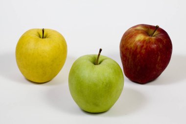 Beyaz arka planda üç sarı, kırmızı ve yeşil elma yan yana yerleştirilir..