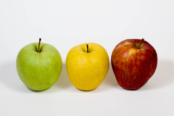Три яблока желтого, красного и зеленого цветов помещены рядом друг с другом на белом фоне.