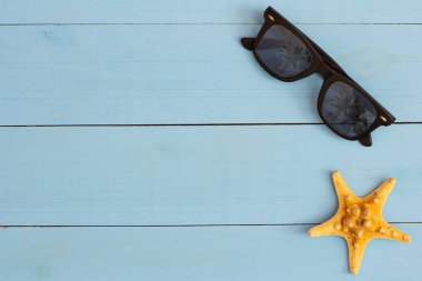 Yaz mevsimi, açık mavi ahşap masada güneş gözlüğü ve deniz yıldızı ile serin bir manzara.
