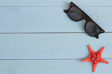 Yaz mevsimi, açık mavi ahşap masada güneş gözlüğü ve deniz yıldızı ile serin bir manzara.