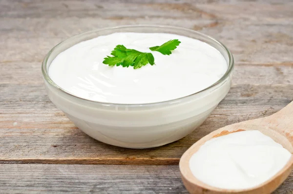 Sour cream in a glass bowl and wooden spoon — Stock Photo, Image