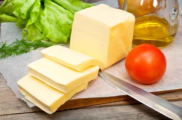 Boter in perkamentpapier en groenten op een houten tafel — Stockfoto