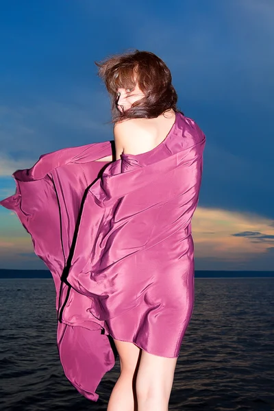 Menina de pé de volta em vestido roxo no fundo do pôr do sol — Fotografia de Stock