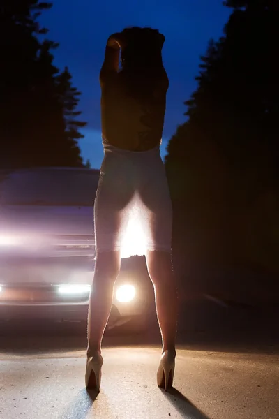 Girl at night on road in headlights ass — Stock Photo, Image