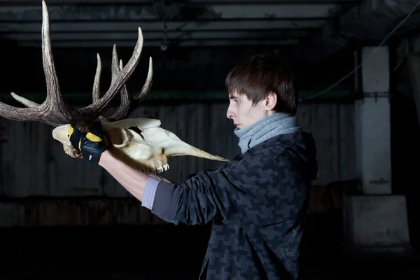 Young man with a sharp deer skull in a dark basement — Stock Photo, Image