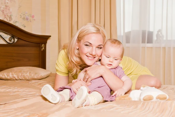 Giovane madre con la sua piccola figlia che gioca sul letto a casa — Foto Stock