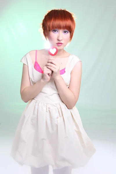 Девушка с рыжими волосами с леденцом в белом платье на светлом фоне — стоковое фото