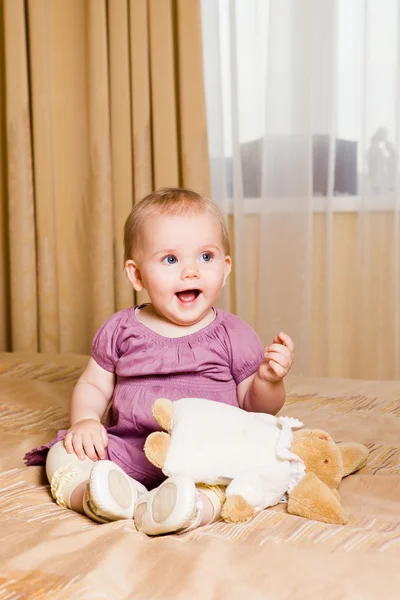 Skrattar lite flicka sitter på sängen med leksak — Stockfoto