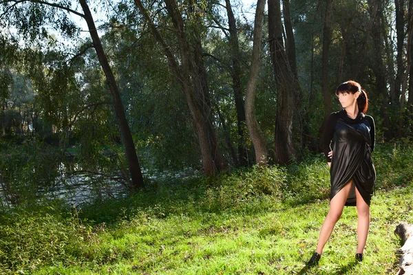 Meisje in zwarte jurk die zich voordeed op glade van bos — Stockfoto