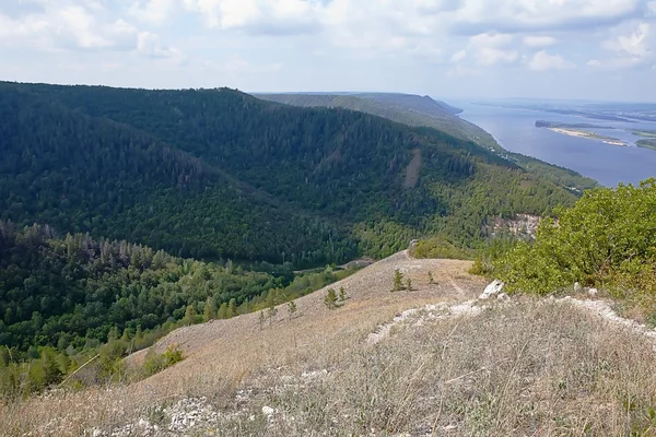 Fragment of rock against mountains with trees horizontally — Stock Photo, Image