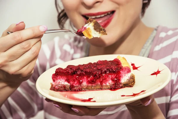 Young joyful woman is tasting a piece of cheesecake with raspber — Stock Photo, Image
