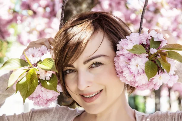 Unga kaukasiska kvinna poserar med blommande sakura träd, skönhet — Stockfoto