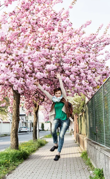 Young caucasian woman is jumping under the flowering sakura tree — Stock Photo, Image