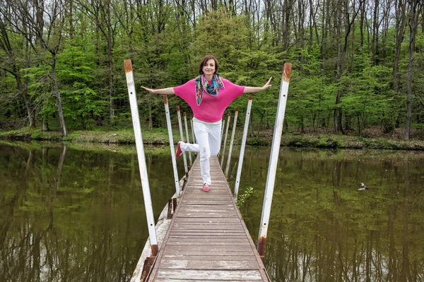 Joven mujer alegre está posando en el puente con el bosque behin — Foto de Stock