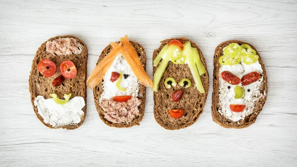 Grappige gezichten gemaakt van brood, boter, tonijn, worst, wortel — Stockfoto