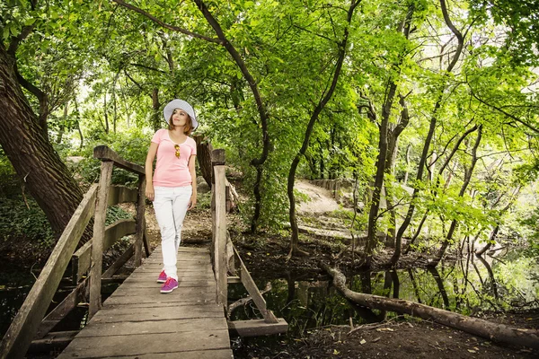 Giovane donna giovane con cappello da sole in posa sul ponte di legno — Foto Stock