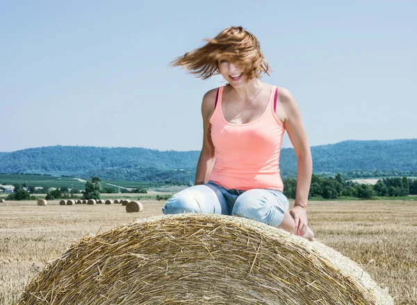 Young crazy caucasian woman sits on the stack of straw and throw — Stock Photo, Image