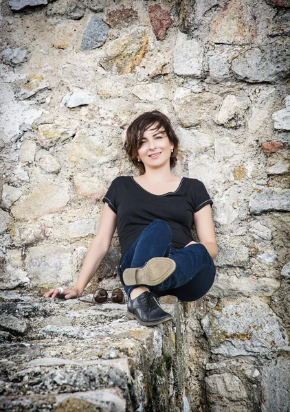 Mooie glimlachend brunette poseren op de stenen muur — Stockfoto