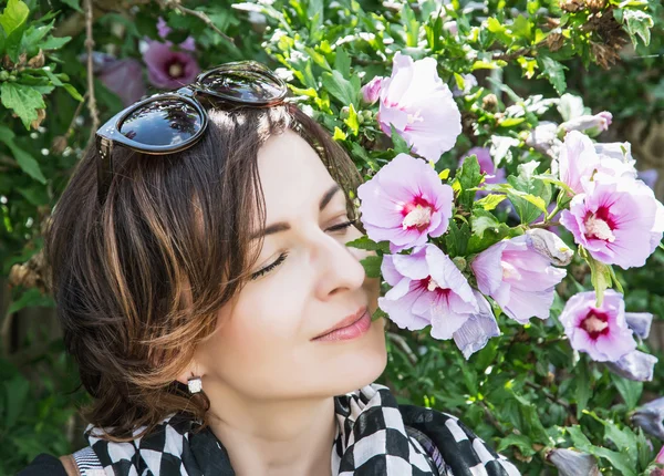 Mladá žena Kavkazský sniffs růžové květy v parku — Stock fotografie