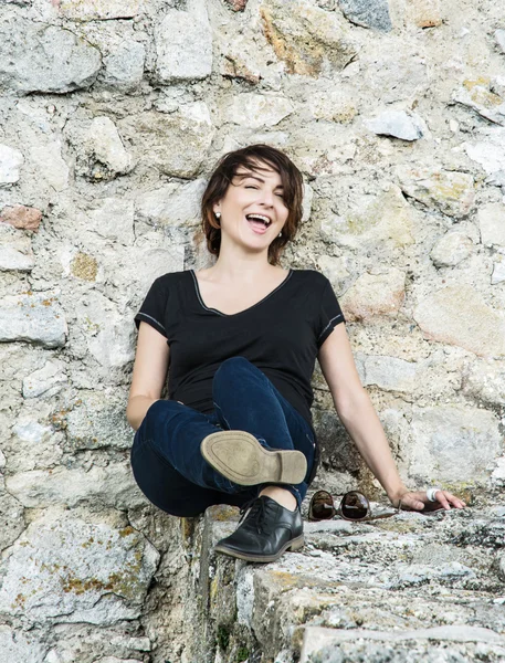 Linda mulher morena sorridente posando na parede de pedra — Fotografia de Stock