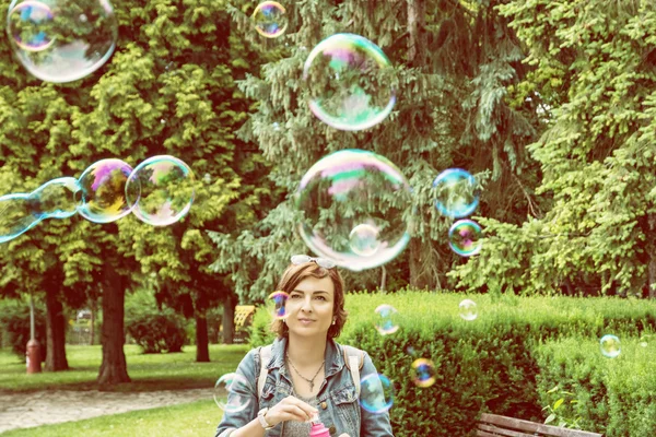 Young caucasian woman blowing soap bubbles in the city park — Stock Photo, Image