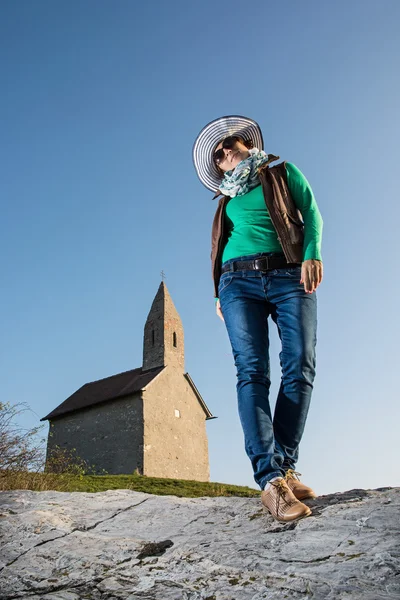 Posing young woman in a stylish hat and an old romanesque church — Stock Photo, Image