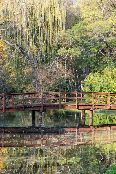 Dřevěný most přes zrcadlené rybník v podzimním parku — Stock fotografie